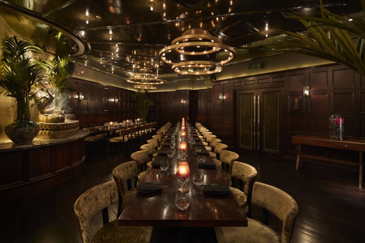 Elegant Tattu Manchester restaurant with long dining tables, dim lighting, candles, chandeliers, and rich wood paneling on walls.