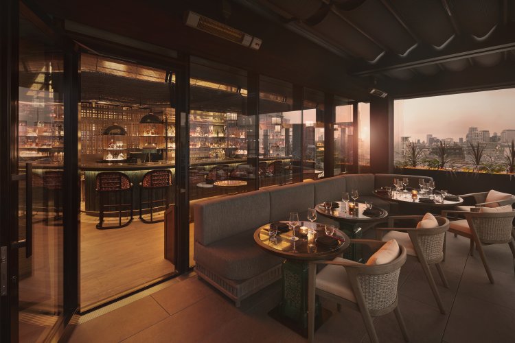 Chic restaurant with city views, modern decor, outdoor seating, cozy sofas, and tables set for dining at sunset.