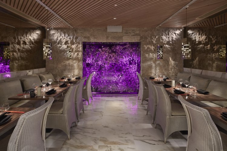 Tattu Restaurant is an upscale Chinese dining establishment featuring elegant decor, marble floors, cushioned seating, and a wall illuminated by purple lighting.