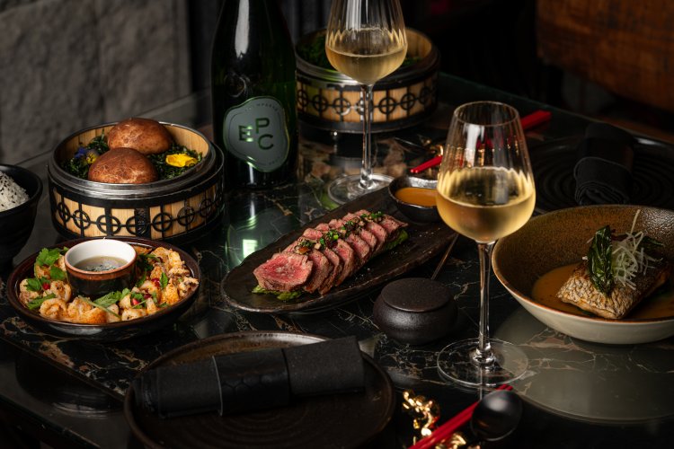 A luxurious dining setup with various gourmet dishes, wine glasses, and a bottle on a dark marble table.